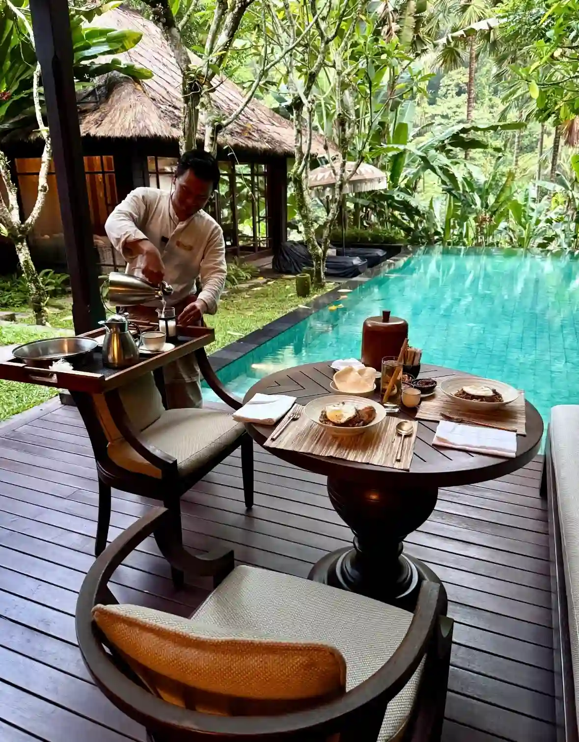 A butler serving breakfast beside a private pool villa at Mandapa in Ubud